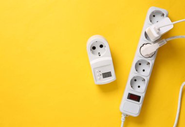 Elektrik uzatma kablosu ve fünyesi ve sarı arka planda elektrik prizi.