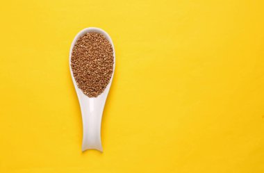 Sarı zemin üzerinde çiğ karabuğday bulunan seramik kaşık