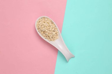 Mavi-pembe arka planda çiğ yulaf ezmeli seramik kaşık. Üst görünüm