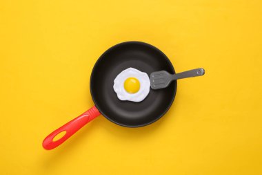 Sarı arka planda çırpılmış yumurtalı plastik oyuncak kızartma tavası