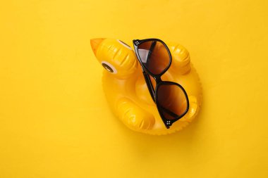 Sarı arka planda güneş gözlüklü şişme ördek. Minimum yaz konsepti. Üst görünüm.