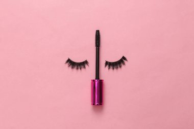 Sahte kirpikler ve pembe arka planda rimel ile kirpik fırçası. Yaratıcı düz yatak, güzellik konsepti