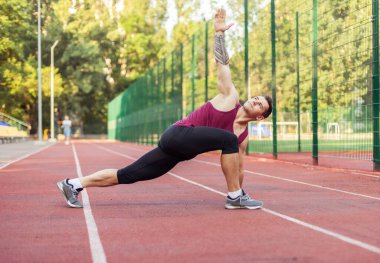 Atletik kaslı adam antrenmandan önce stadyumda ısınıyor. Sağlıklı yaşam tarzı