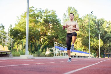 Çıplak gövdesiyle atletizm antrenmanı yapan atletik bir adam stadyuma koşmadan önce ısınıyor. Sağlıklı yaşam tarzı