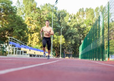 Stadyumda çıplak gövdeli atletik bir erkek koşuyor. Kaslı koşucu ya da koşucu. Sağlıklı yaşam tarzı