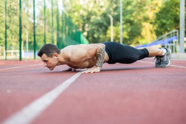 Çıplak gövdeli genç atletik bir adam stadyumda şınav çekiyor..