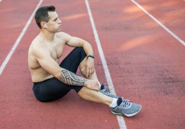 Stadyumda otururken çıplak gövdesi dinlenen yorgun genç bir sporcu.