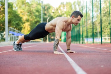 Çıplak gövdeli genç atletik bir adam stadyumda şınav çekiyor..