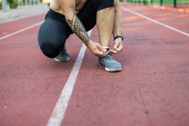 Stadyumda spor ayakkabılarının bağcıklarını bağlayan atletik bir adam.