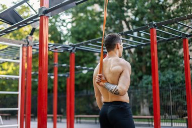 Spor sahasında spor lastiğiyle çıplak gövde trenleri olan atletik erkek sporcu. Açık hava egzersizi.
