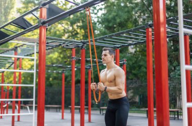 Spor sahasında spor lastiğiyle çıplak gövde trenleri olan atletik erkek sporcu. Açık hava egzersizi.