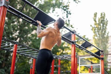 Çıplak gövdeli atletik erkek sporcu antrenman sahasında kendini yukarı çekiyor. Açık hava egzersizi.