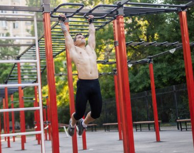 Çıplak gövdeli atletik erkek sporcu antrenman sahasında kendini yukarı çekiyor. Açık hava egzersizi.