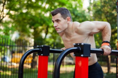 Çıplak gövdeli atletik adamlar antrenman alanındaki düz olmayan parmaklıklara şınav çekerler.