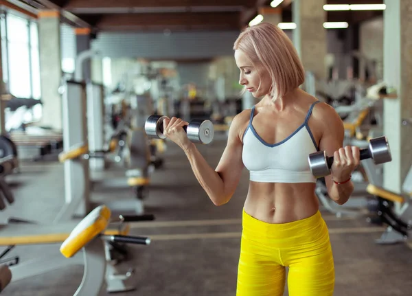 근육질의 여자는 현대식 체육관에서 방울을 사용하여 이두근을 시킨다 아름다운 — 스톡 사진