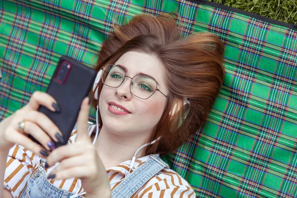 Молодая Веселая Женщина Слушает Музыку Наушниках Пользуется Смартфоном Лежа Одеяле — стоковое фото