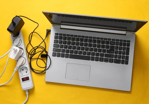Laptop, Electrical Extension cord with different plugs and adapters. Yellow background. Top view