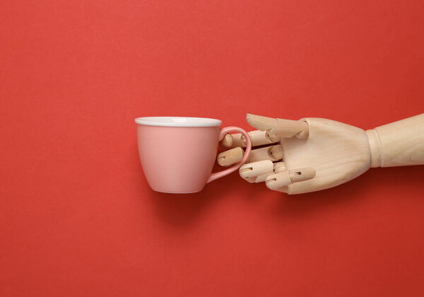 Wooden hand holding empty tea cup on red background