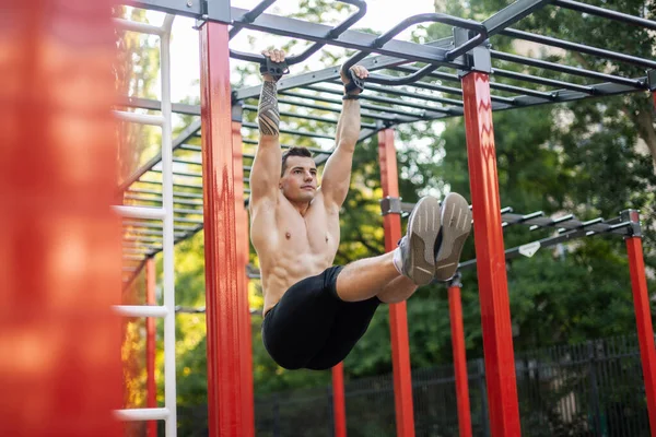 Çıplak gövdeli atletik erkek sporcu karın kaslarını egzersiz alanında bacaklarını kaldırarak çalıştırıyor. Açık hava egzersizi.