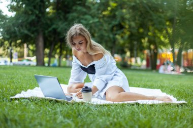 Parkta ekose üzerinde dizüstü bilgisayarla çalışan mutlu, güzel bir kadın.