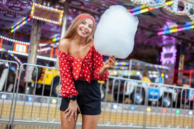 Pamuk şekerli sevimli bir kadın bir eğlence parkının ortasında duruyor. Parlak renklerle, olumlu ve neşeli, mutlu ve iyimser duygularla.