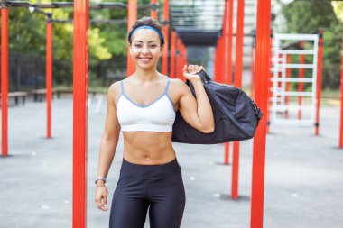 Güzel gülümseme, spor sahasında çantası olan genç kaslı kadın.