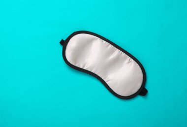 Turkuaz arka planda uyku maskesi. Üst manzara, düz yatış. Gerçekçi rüyalar kavramı. Uyku için aksesuarlar. Asgari stil... Boşluğu kopyala