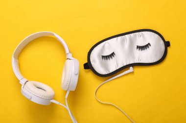 Rahatlatıcı uyku müziği. Sarı arka planda kirpikli ve kulaklıklı uyku maskesi.
