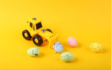 Sarı arka planda paskalya yumurtası olan oyuncak sarı forklift..