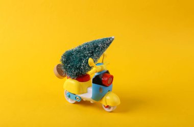Sarı arka planda Noel ağacı olan bir scooter. Teslimat konsepti, Noel kompozisyonu