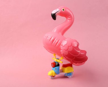 Scooter pembe arka planda şişme flamingo taşıyor. Yaz tatili
