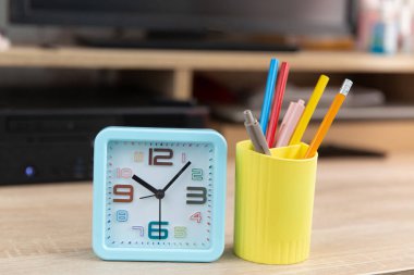 Bilgisayar masasında kırtasiye malzemesi olan çalar saat ve bardak.