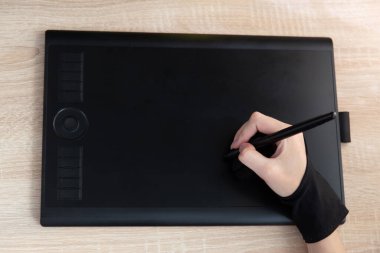 Kadın eli masanın üzerinde grafik tableti ile çalışıyor. Tasarımcı veya rötuş işi