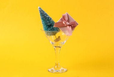 Noel ağacı ve hediye kutuları sarı arka planda kokteyl bardağında. Yaratıcı bir fikir. Asgari Noel partisi konsepti.