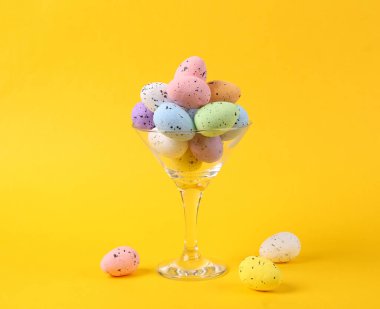 Sarı arka planda renkli yumurtalı kokteyl bardağı. Yaratıcı bir fikir. Asgari Paskalya konsepti. Sanat kavramı, düzen