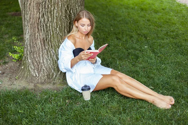 Mladá Atraktivní Žena Čtení Knihy Zatímco Sedí Trávě Opírající Strom — Stock fotografie