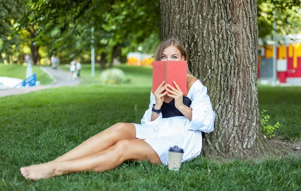 Mladá Atraktivní Žena Knihou Zatímco Sedí Trávě Opírající Strom Parku — Stock fotografie