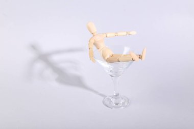 Gri arka planda, kokteyl bardağında tahta kukla. Yaratıcı bir fikir. Asgari parti konsepti, yerleşim