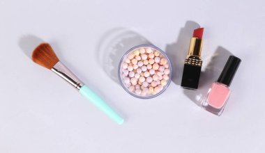 Gri arka planda makyaj ürünleri. Tırnak cilası, toz topları, makyaj fırçaları ve ruj.