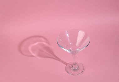 Pembe arka planda uzun trend gölgesi olan boş kokteyl bardağının minimal görüntüsü