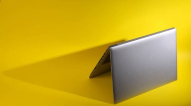 Sarı arka planda uzun gölgeli katlanmış bir laptop. En küçük yerleşim