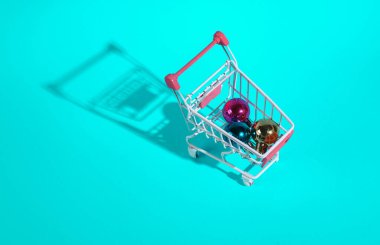 Turkuaz arka planda Noel oyuncakları olan mini alışveriş arabası.