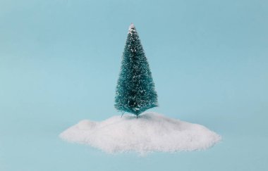 Turkuaz arka planda kar yığınında bir Noel ağacı. En küçük yerleşim