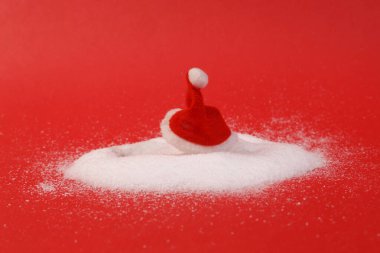 Kar yığınındaki Noel Baba şapkası. Kırmızı arka plan. Noel düzeni