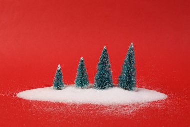 Kırmızı arka planda kar yığınındaki Noel ağaçları. En düşük kış düzeni