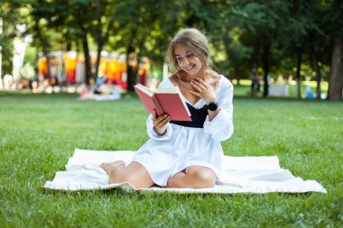 Parkta ekose kitap okuyan güzel genç bir kadın.