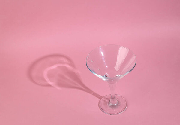 Minimalistic shot of empty cocktail glass with long trending shadow on pink background