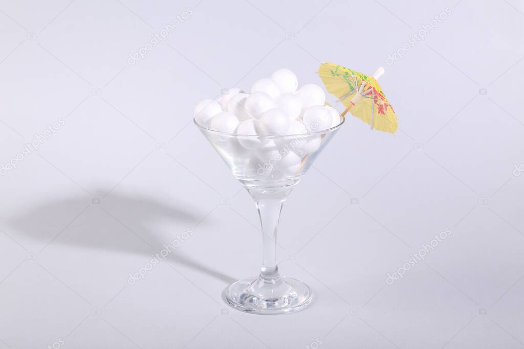 White balls and umbrella in cocktail glass on gray background. Fresh idea. Minimal party concept, creative layout