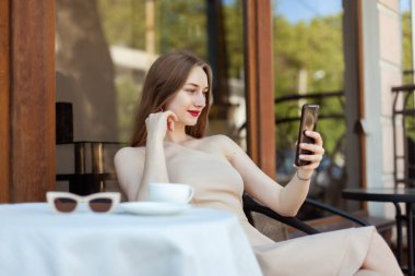 Açık kafedeki masada otururken akıllı telefon kullanan gülümseyen kadın.