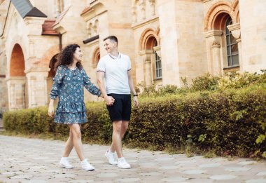 Birbirine aşık genç bir çift el ele tutuşup dışarıda yürüyor.